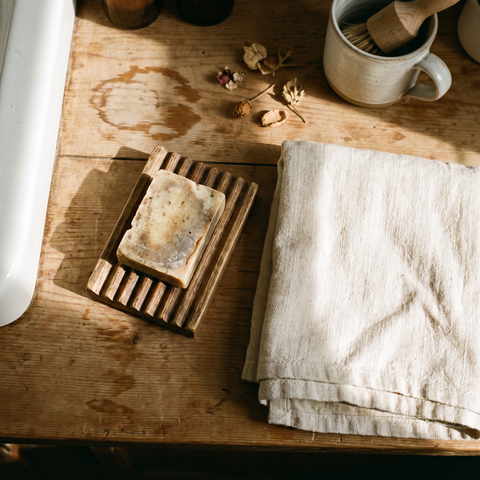 Soap bar on a wooden soap saver next to a linen towel, lifestyle photo